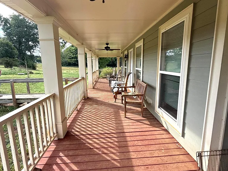 A Wraparound Porch With Grazing Cattle Next Door